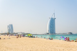 People are enjoying a sunny day on a beach in front of the Burj al Arab hotel in Dubai, UAE