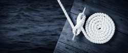Boat Rope Secured To Cleat On Wooden Dock With Dark Water Below