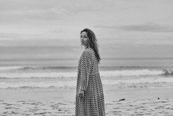 Happy positive modest woman with long hair in long dress standing on sea coast at the beach Filling breeze Holiday vacation