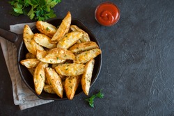 Baked potato wedges with cheese and herbs and tomato sauce on black background - homemade organic vegetable vegan vegetarian potato wedges snack food meal.