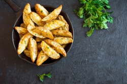 Baked potato wedges with cheese and herbs and tomato sauce on black background - homemade organic vegetable vegan vegetarian potato wedges snack food.