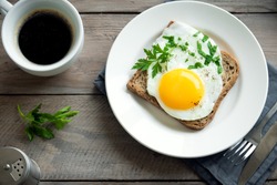 Fried Egg on Wholegrain Toast and cup of Coffee for Breakfast. Fried egg with bread on plate over wooden table, top view, copy space.