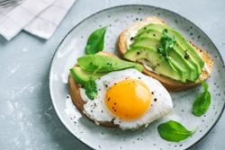 Avocado Sandwich with Fried Egg - sliced avocado and  egg on toasted bread with arugula for healthy breakfast or snack.
