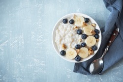Oatmeal porridge with walnuts, blueberries and banana in bowl - healthy organic breakfast, oats with fruits, honey and nuts.