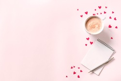 Cup of coffee, open notebook and red hearts on pink beige background, copy space. Minimal flat lay with capuccino coffee and mock up book for Valentine day text, love and romance concept, top view.