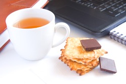 Healthy quick snack (lunch, break) in office. Cup of tea, cookies (biscuits) and chocolate on white desk with computer.