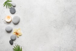 Spa concept on white stone background, palm leaves, flower, candle and zen like grey stones, top view, copy space.