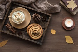 Cozy home and autumn hygge concept. Seasonal autumnal composition with soft plaid, coffee latte, fresh pastry cinnamon bun, candle on wooden, top view, copy space.