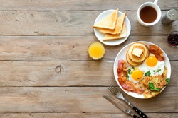 Full American Breakfast on wooden, top view, copy space. Sunny side fried eggs, roasted bacon, hash brown, pancakes, orange juice and coffee for breakfast.