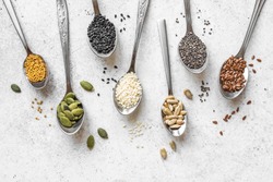 Various Seeds Assortment on white background. Set of  sesame seeds, flax seed, sunflower seeds, pumpkin seed, chia, hemp seeds in spoons, healthy food ingredients, top view, copy space.