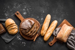 Fresh Bread on black background, top view, copy space. Homemade fresh baked various loafs of wheat and rye bread flat lay.