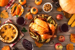 Thanksgiving dinner with chicken, cranberry sauce, pumpkin pie, wine, seasonal vegetables and fruits on wooden table, top view. Traditional autumn holiday food concept.