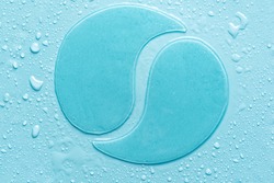 Hydrogel blue eye patches on blue background with water drops close up. Cosmetic moisturizing under eye patches with collagen.