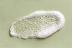 Face cleansing mousse sample. White cleanser foam bubbles on green background. Soap, shower gel, shampoo foam texture closeup.