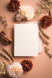 Greeting or invitation blank card, wheat and rose flowers on craft brown background, copy space. Stylish creative autumn fall mock up, autunm holiday celebration concept.