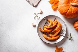 Grilled pumpkin slices with garlic and herbs on white background, copy space. Oven baked pumpkin, seasonal autumn side dish or vegan meal.