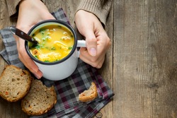 Woman hands holding mug of vegetable soup with parsley and croutons over wooden background - healthy winter vegetarian food