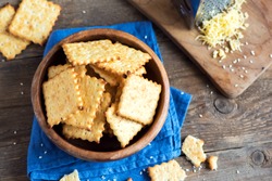 Homemade thin crispy cheesy crackers with sesame seeds in rustic wooden bowl - fresh organic homemade baking cheese crackers snack