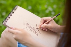 Closeup photo of young woman drawing with pencil on plain air, outdoors. Art education, talented students.