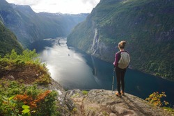 Young female hiker standing in awe and admiring 7 sisters waterfall in Norway, Geiranger Fjord, o a summer day