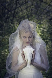Mystic stories, blond woman in a wedding dress and ring holding the animal's skull. Magic and witchcraft. Girl want to get married. Concept - cover for the book.