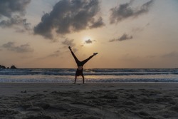Silhouette of a young woman standing on her hands on the beach at sunset.