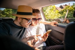 Young cheerful happy couple of travelers sitting in car looking at smartphone screen, travel comfort safety taxi concept