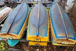 Several old rowing boats are piled up for the winter season. The blue and yellow cases are made of fiberglass. Autumn. 