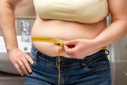 Cropped midsection of an obese woman measuring her waist with a measuring tape in the bathroom