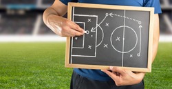 hand of a football coach drawing a tactics of soccer game with white chalk on blackboard at stadium background
