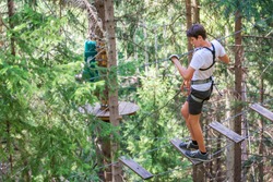 Teenager having fun on high ropes course, adventure, park, climbing trees in a forest in summer