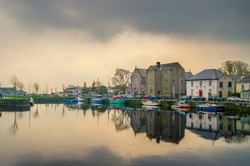 Cloudy sunset over the Galway Dock, with fishing boats and Dominican church. Water reflection.