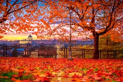 Rome, Vatican - autumn park bench with red leaves and St Peter's basilica and Rome in the background at sunset
