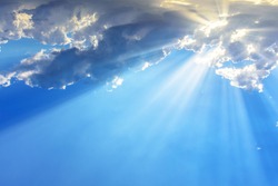 Sun light rays or beams bursting from the clouds on a blue sky. Spiritual religious background.
