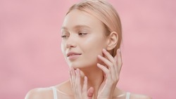 Young slim gorgeous blond European woman touches her face against pink background | Face skin care commercial
