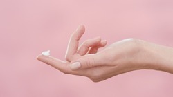 Female hand with cosmetic cream on her finger on pink ripple background | Skincare cream commercial concept