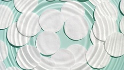 Drop makes wave circles on water surface on pale green background with cotton pads | Background shot for makeup remover commercial
