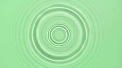 Drop falls down on water surface creating rings on green background | Beauty background shot for skin care cosmetics commercial