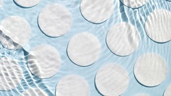 Poured water splashing and making ripples over cotton pads arranged in rows on blue background | Skin care product background, cleansing lotion commercial