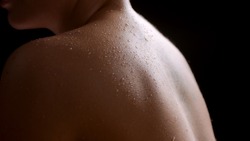 Big close-up shot of good-looking young slim white-skinned woman's wet bare shoulders on black background  Wet skin texture shot for flawless skin concept