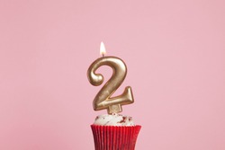 Number 2 gold candle in a cupcake against a pastel pink background