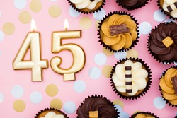 Number 45 gold candle with cupcakes against a pastel pink background