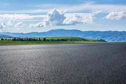 Empty asphalt road and green grassland and mountain under blue sky 