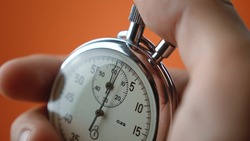 Close-up of male hand holding analogue stopwatch on orange background. Time start with old chronometer man presses start button in the sport concept. Time management concept.