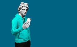 Modern art collage. Concept portrait of a man  holding mobile smartphone using app texting sms message. Gypsum head of of Apollo. Man in suit. On a blue background.