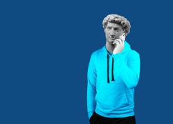 Modern art collage. Concept portrait of a man  holding mobile smartphone using app texting sms message. Gypsum head of of David. Man in suit. On a blue background.
