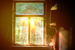 The bright rays of the sun illuminate the room through the old window of the village house.