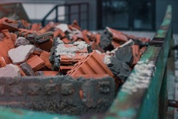 Green metal skip full of broken brick and stone material standing on construction site. Demolition and removal work concept.