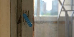 outdated wooden window handle of blue colour against blurry balcony with metal equipment and cityscape close view