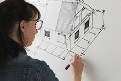 Close-up of a young female architect drawing a sketch for a new famaly home project. Concept of work on technical drawings